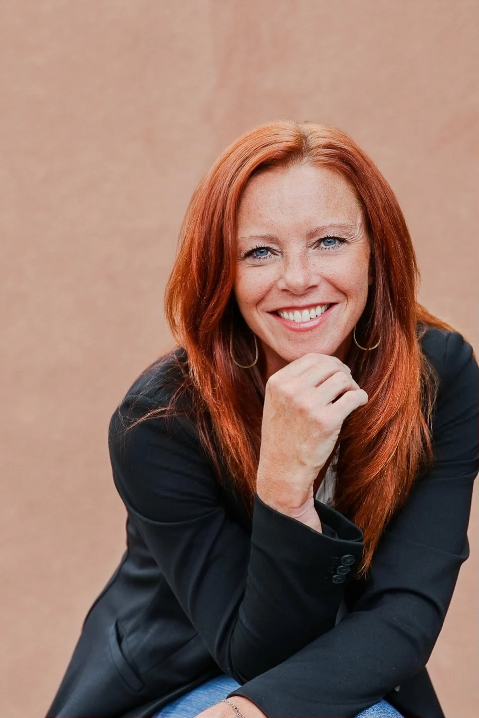 Angela smiling in a black blazer with her hand resting beneath her chin